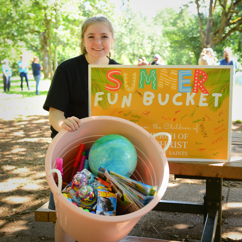 Woman behind a sign that reads, "fun bucket" and a bucket of toys