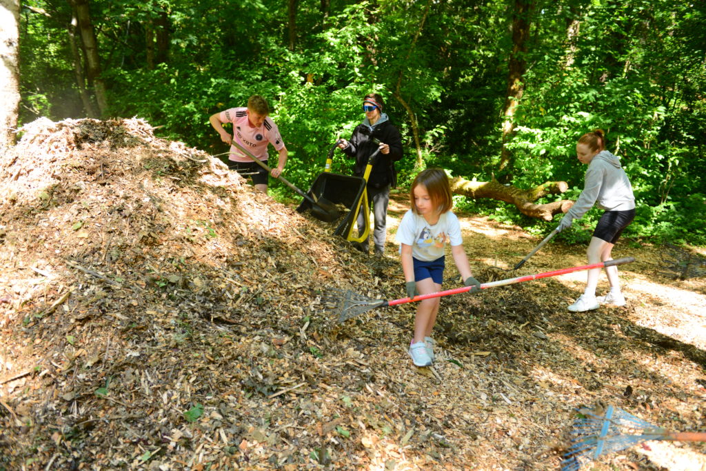 Girl with rake helps three other women with bark mulch at local park