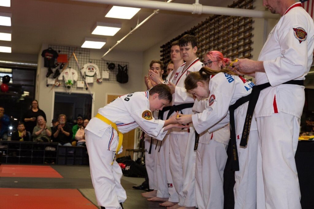 Student receives belt from Coach while other coaches look on