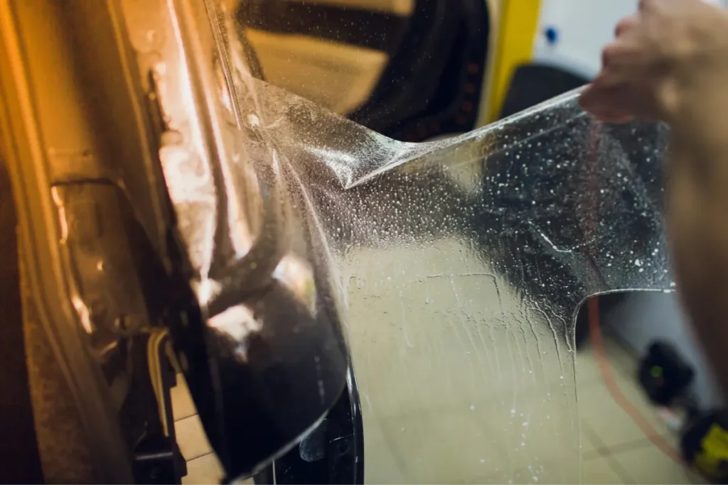 Technician peeling clear paint protection film off a car panel during service.