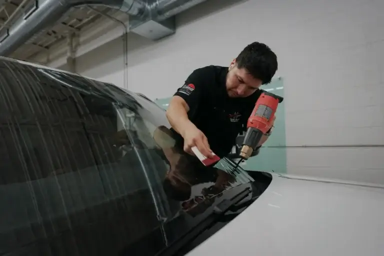 Technician using a heat gun and squeegee for window tinting Elmhurst IL service.