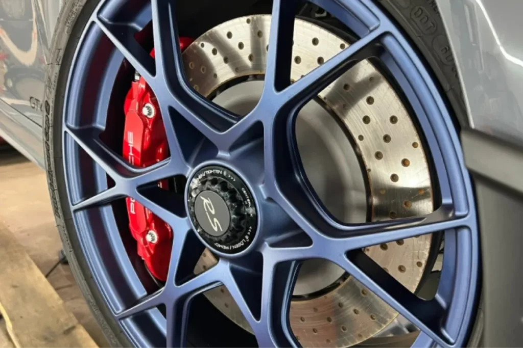 Clean Porsche wheel with blue rim and red brake caliper for auto detailing in Charlotte, NC.