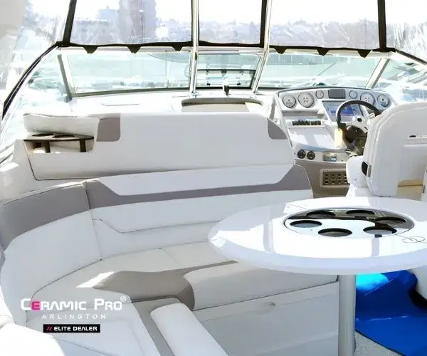 view of a luxury boat deck featuring clean white vinyl seating, a central pedestal table, and a helm station.