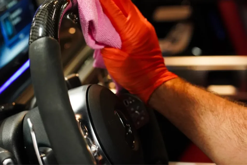 Gloved hand cleaning a steering wheel with a microfiber cloth during interior car detailing.