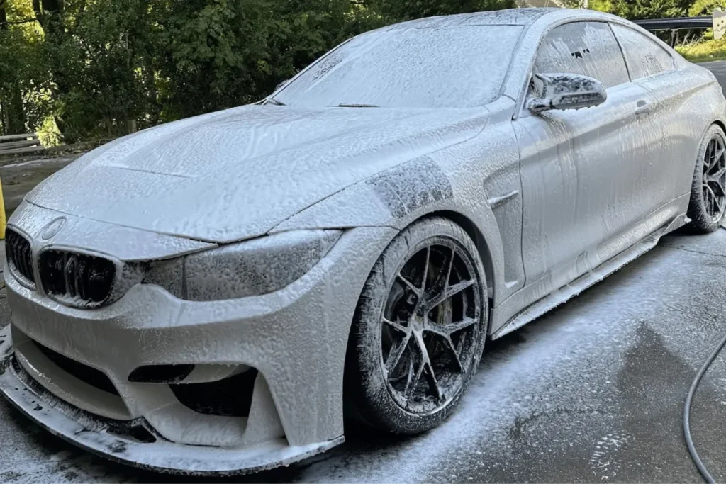 White BMW coupe covered in thick foam during a mobile detailing service.