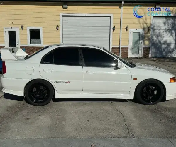 Side profile view of a white Mitsubishi Lancer Evolution IV with black wheels parked outside Coastal Coating.