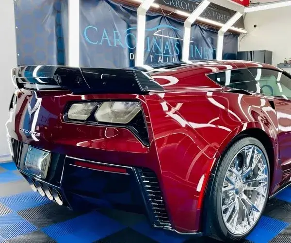 view of a metallic red Chevrolet Corvette sports car with chrome wheels parked under overhead LED garage lights