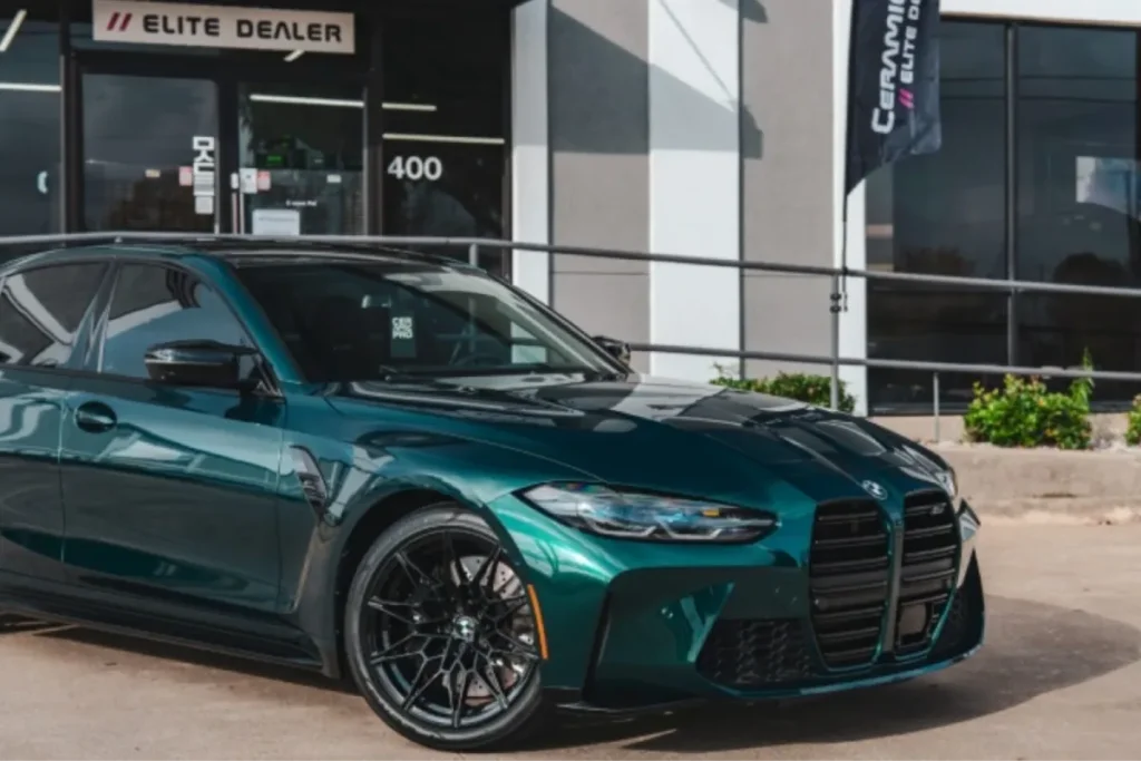 Glossy dark green luxury sedan parked outside a vehicle detail shop with paint protection film.
