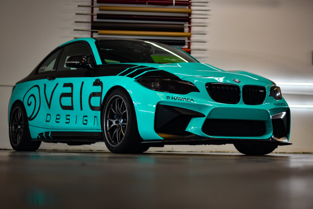 Bright turquoise BMW sports coupe with black accents and custom vinyl graphics parked outside a building.