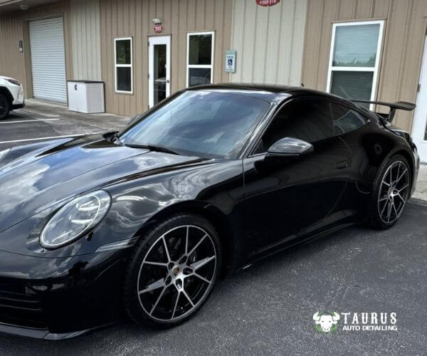 Close-up front three-quarter view of a black Porsche sports car showing dark window tinting.