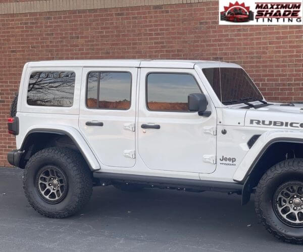 Side profile of a white four-door Jeep parked against a brick wall.